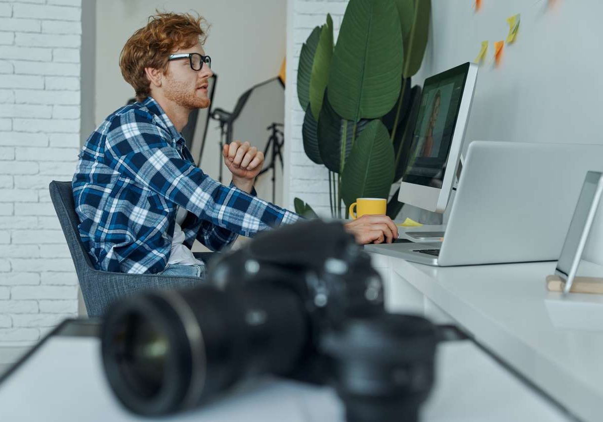 Confident young man using computer while digital camera laying on foreground